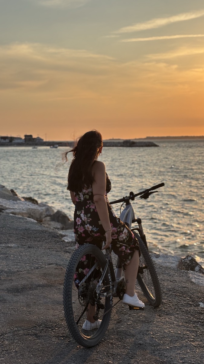 A rider on an eBike on the Costa da Caparica seafront looking out over the water at sunset