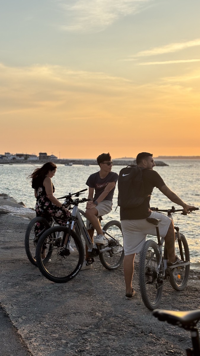 Three riders resting on their eBikes by the sea, watching an orange sunset at Costa da Caparica