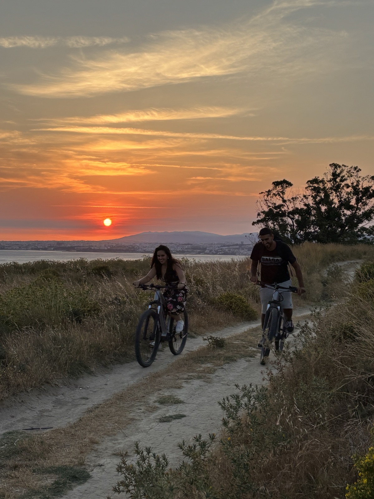 Two riders on eBikes on a coastal trail at sunset during the Lisbon's Hidden Gem tour in Costa da Caparica