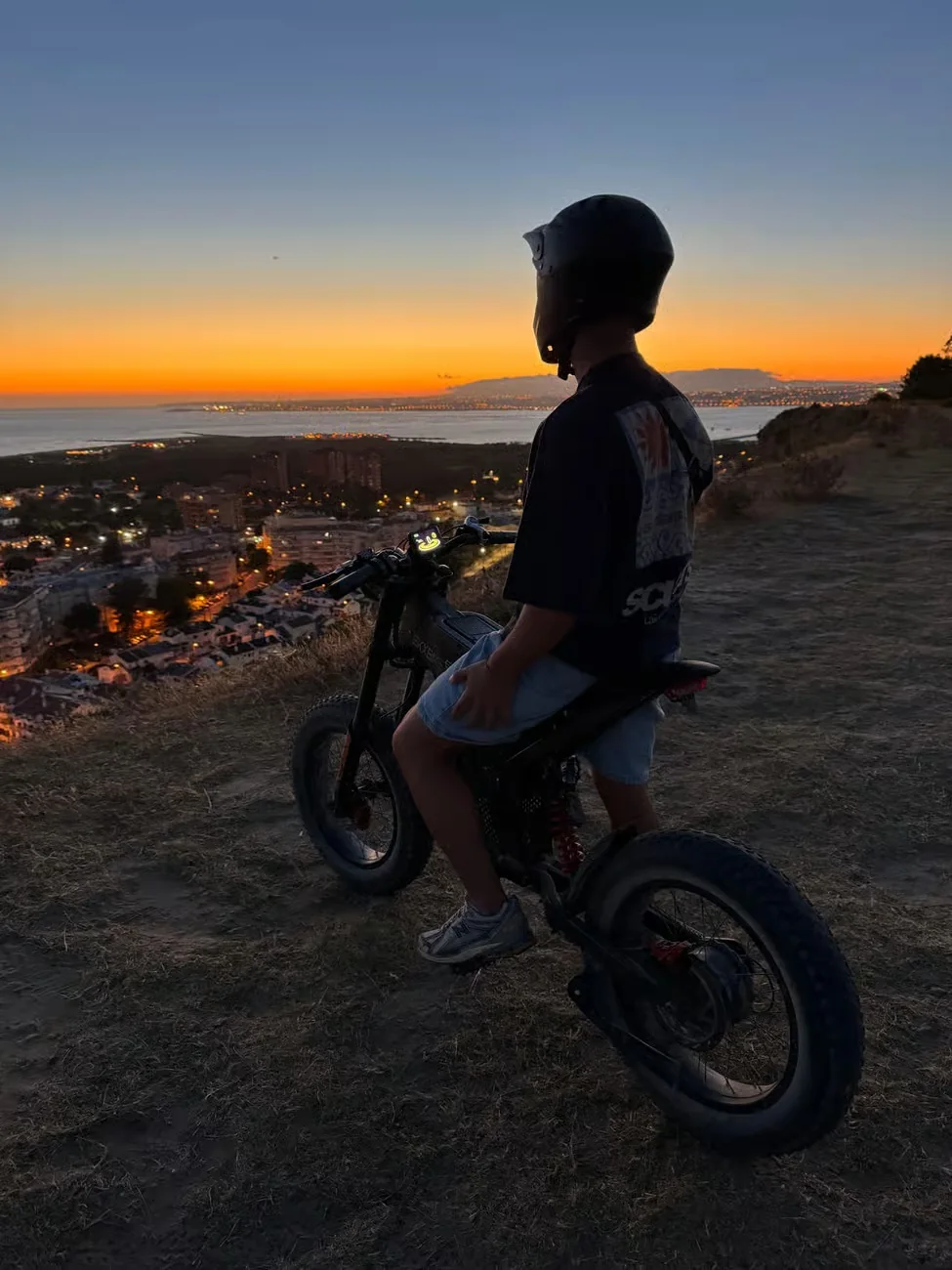 Helmeted rider overlooking Costa da Caparica and the Atlantic coast at sunset during a guided eBike tour