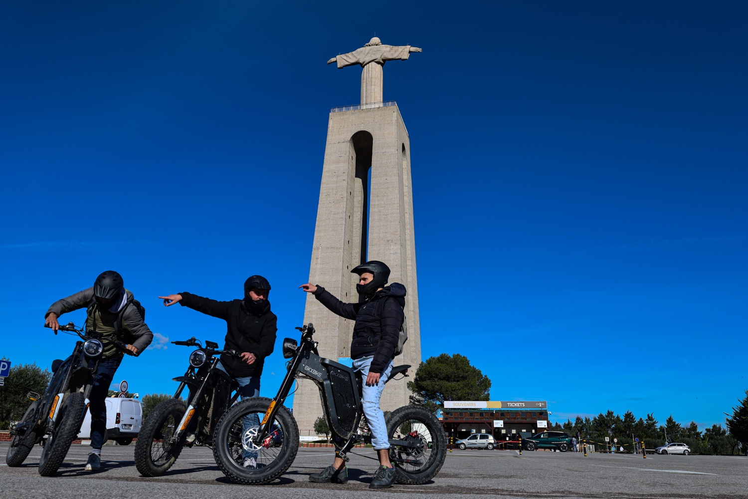 Three riders with their eBikes in front of the Cristo Rei monument in Almada